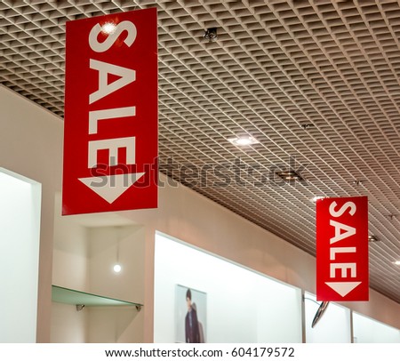 few red vertical sale posters with white letters hang from grid ceiling in big shop in sale season. sale poster board at fashion clothes shopfront