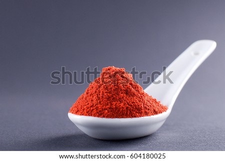 Ground red pepper in a white spoon on a dark background