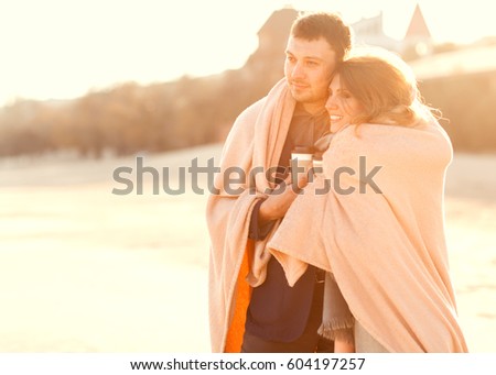 Couple at the beach drinking tea wrapped in a plaid at sunset