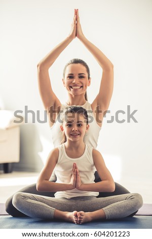 Beautiful young woman and her charming little daughter are smiling while doing yoga together at home