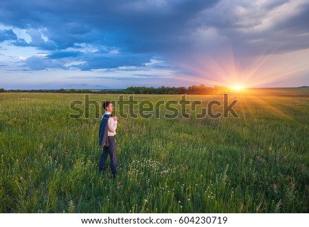 Businessman in elegant suit with his jacket hanging over his shoulder standing in field looking into the distance under a majestic evening sky with a setting sun.