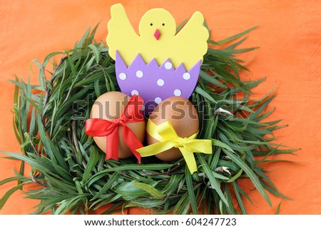 easter decoration: yellow eggs and hand made hatched chicken in eggshell in green grass twigs nest on orange background with copy space