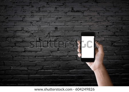 Man holding blank screen of a smartphone at the old black brick wall.
