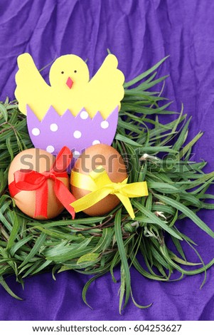 easter decoration: yellow eggs and hand made hatched chicken in eggshell in green grass twigs nest on purple background with copy space