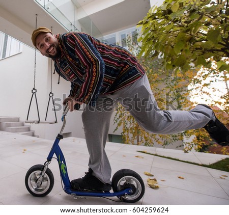 Happy playful adult man on scooter in front of his modern house