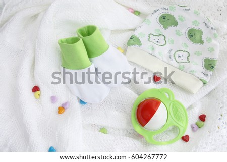 green knitwear newborn baby booties and hat with colorful rattle on crocheted blanket white background with colorful hearts with copy space
