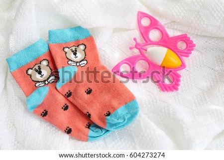 red knitwear newborn baby socks with bears and colorful pink butterfly rattle on crocheted blanket white background with copy space