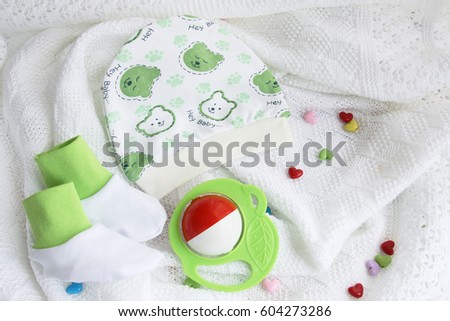 green knitwear newborn baby booties and hat with colorful rattle on crocheted blanket white background with colorful hearts with copy space