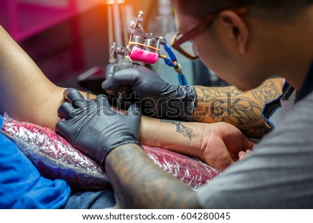 Close up tattoo artist demonstrates the process of getting black tattoo with paint. Master works in black sterile gloves