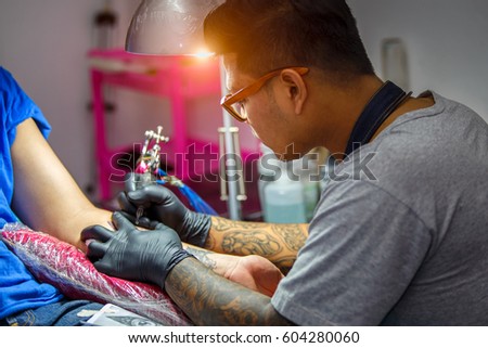 Close up tattoo artist demonstrates the process of getting black tattoo with paint. Master works in black sterile gloves