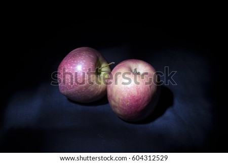 Pair of Pink Lady apples darkness illuminated by un LED light beam.