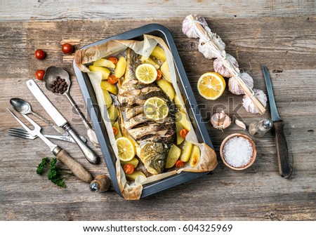 Appetizing baked fish, covered with juicy lemons, garlic and salt on side, topview