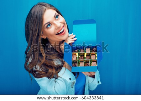 Surprised girl holding box with chocolate candies. Young woman portrait with sweets.