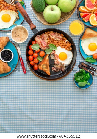 Healthy breakfast table  - fried egg, beans, tomatoes, bacon, toast various fruits, juice and coffee on a rustic table with copy space, top view 