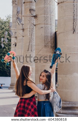 Two beautiful girl with long hair in a summer city with skateboard