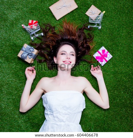 beautiful young woman near gifts and shopping carts lying on the wonderful green grass background