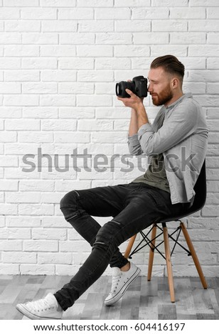 Handsome photographer sitting on chair near light brick wall