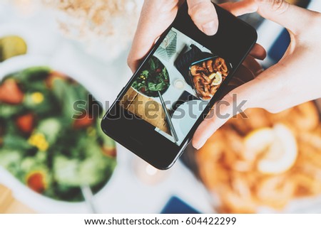 Closeup shot of female hands holding smartphone and taking a photo, top view of hipster girl taking a picture of food by smartphone
