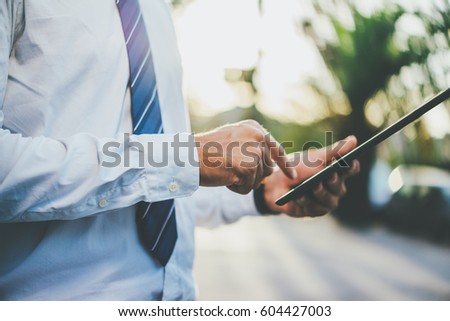 Closeup image of male manager using digital tablet outdoors, professional businessman typing text information in internet during a break about financial department, filtered image