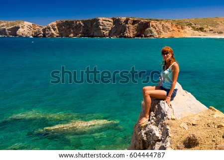 girl is sitting on a cliff face over the sea. tourist girl admires the sea view. Travel Concept. Time for rest and relaxation. Girl tourist sits on a high mountain stone. Clean sea and wild seascape
