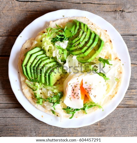 Poached egg, fresh avocado slices, salad, chinese cabbage, dried herbs, sauce on a tortilla. Tasty tortilla with filling on a plate isolated on old wooden background. Vegetarian meal. Top view