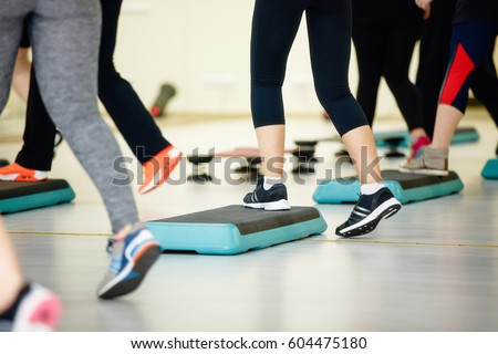 Women doing aerobic class with steppers to people group on fitness center detail of raised feet during aerobic step exercise at gym aerobics and people concept people working out with steppers in gym. Royalty-Free Stock Photo #604475180
