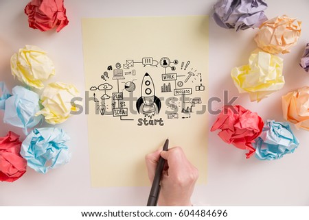 Close up of a hand drawing a rocket sketch on a piece of paper with paper balls lying around