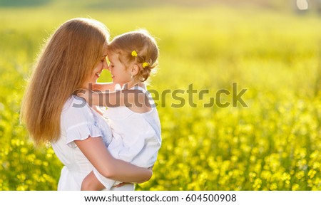Happy family mother and child daughter embrace on yellow flowers on nature in summer
