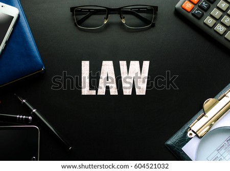 Black chalkboard with business accessories (notepad, magnifying glass, fountain pen, tablet, phone, glasses and calculator) and text LAW. Top view.