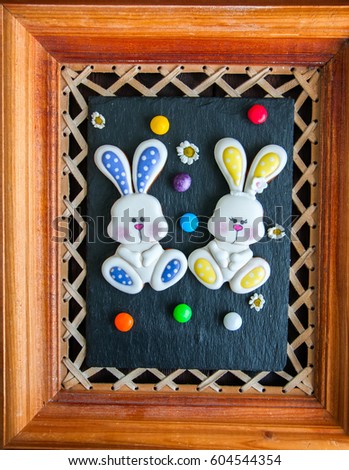 Decorated Easter Bunny Cookies Colored Candies Chamomiles over black stone board in a wooden frame.  Easter concept.