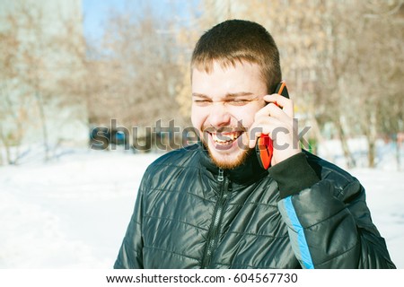 Telephone calls men. The guy is talking on cell phone street in winter,dressed  warm clothes, holds his hand phone at ear, bright orange sheath case, emotionally smiling