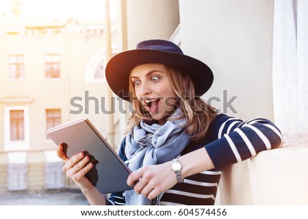 Attractive young female tourist chatting with colleagues talking about her adventure abroad while standing on cityscape on sunny day using tablet pad.