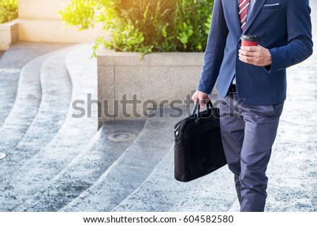 full length picture of a young business man walking forward with a briefcase in one of his hands and coffee cup.