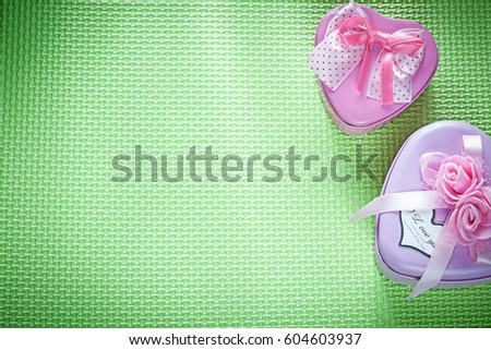 Metal heart-shaped gift boxes with ribbons on green surface copy space holidays concept.