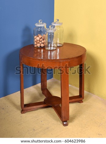 Retro Furniture Still Life of Small Round Wood Side Table with Collection of Three Glass Jars - One with Nuts - in Room with Blue and Yellow Walls