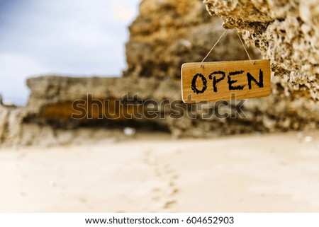 Close up of open sign on hanging banner on the rock with wild beach background.