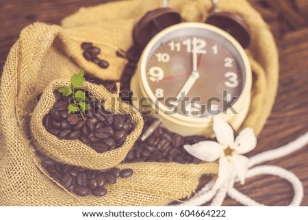 In selective focus of Vintage brown clock face and and coffee beans in sack fall on wooden table outdoor background. Coffee break for relax time concept. vintage effect style pictures