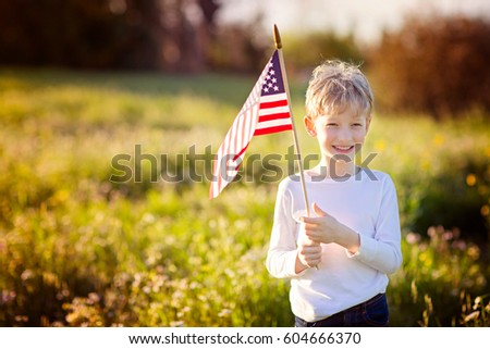 happy proud caucasian boy holding american flag celebrating 4th of july outdoors