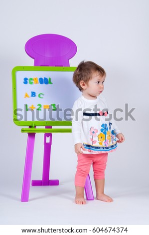 A little girl is standing near the board with letters and numbers. The school is written on the blackboard.
