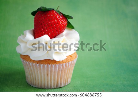 Cupcake with whipped cream, fresh strawberry on green background. Picture for a menu or a confectionery catalog.