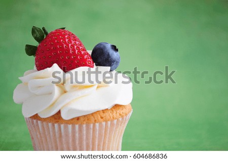 Cupcake with whipped cream, fresh strawberry, blueberry on green background. Picture for a menu or a confectionery catalog.