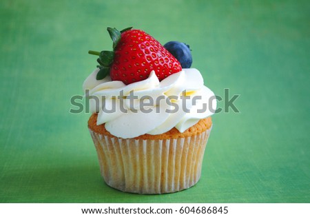Cupcake with whipped cream, fresh strawberry, blueberry on green background. Picture for a menu or a confectionery catalog.