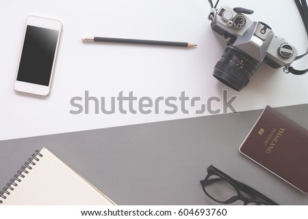 Flat lay design of work desk with notebook, camera, pencil, eye glasses, passport and smartphone on white and gray background. Work and travel concept.