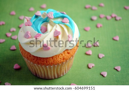 Cupcake with whipped cream and pink confectionery sprinkling In the form of hearts on green background. Picture for a menu or a confectionery catalog.