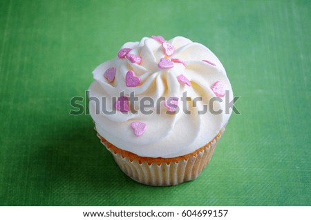 Cupcake with whipped cream and pink confectionery sprinkling In the form of hearts on green background. Top view. Picture for a menu or a confectionery catalog.