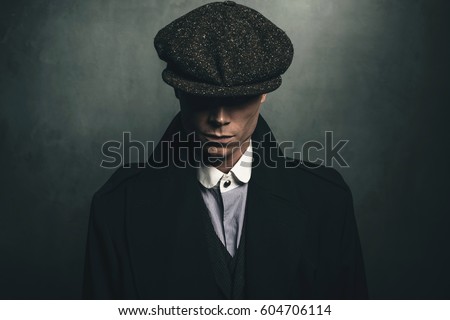 Mysterious portrait of retro 1920s english gangster with flat cap. Royalty-Free Stock Photo #604706114