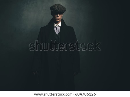 Mysterious retro 1920s english gangster with flat cap and black coat. Royalty-Free Stock Photo #604706126
