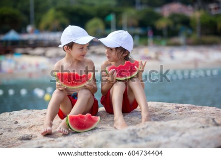Two little children, boy brothers, eating watermelon on the beach, summertime