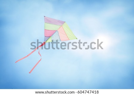 angle view of a colorful kite flying with waving red bow in a deep blue sky with the light of the sun