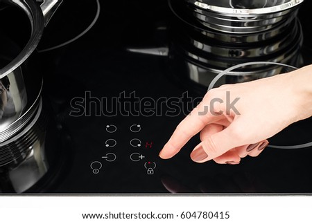 Female hand turns on electric hob closeup, finger presses button on modern induction cooker, Metal steel saucepan in kitchen with stove top panel, modes of cooking surface, Domestic equipment,